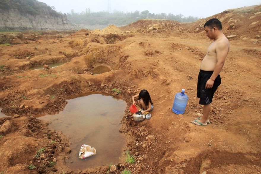 girl collects water from a puddle at a dried-up reservoir as her father stands beside her in Baofeng county