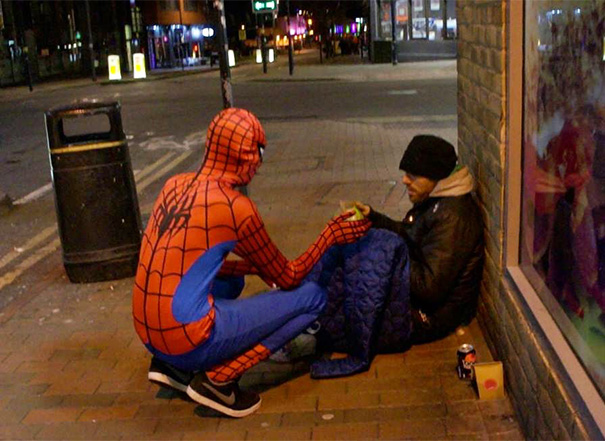 Un bărbat îmbrăcat în Spiderman hrănește oamenii străzii pe timpul nopții
