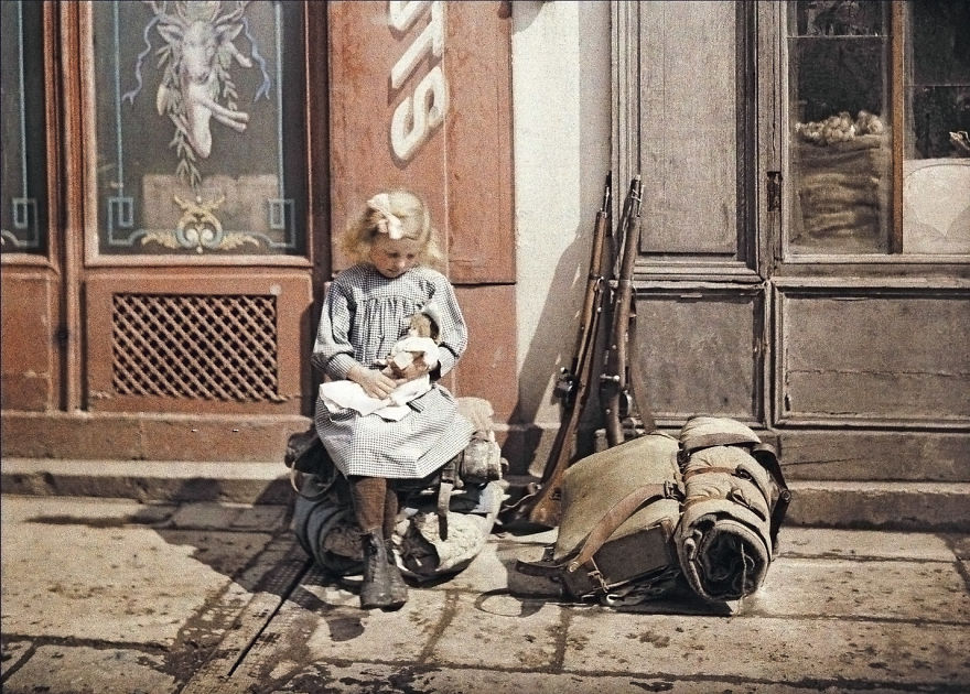 Uma menina segura uma boneca ao lado do equipamento de soldados em Reims, França, 1917