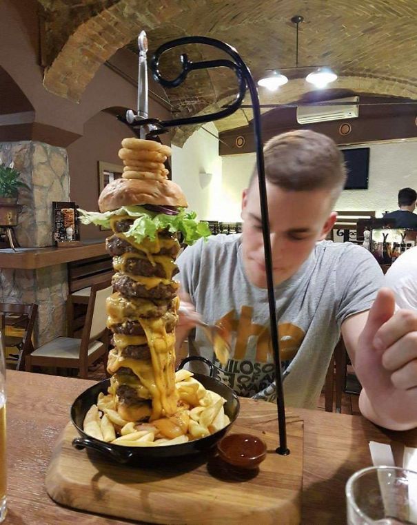 Terrible Bun: Meat Ratio And Precariously Tall Burger On A Skillet On A Board With A Sword Through It