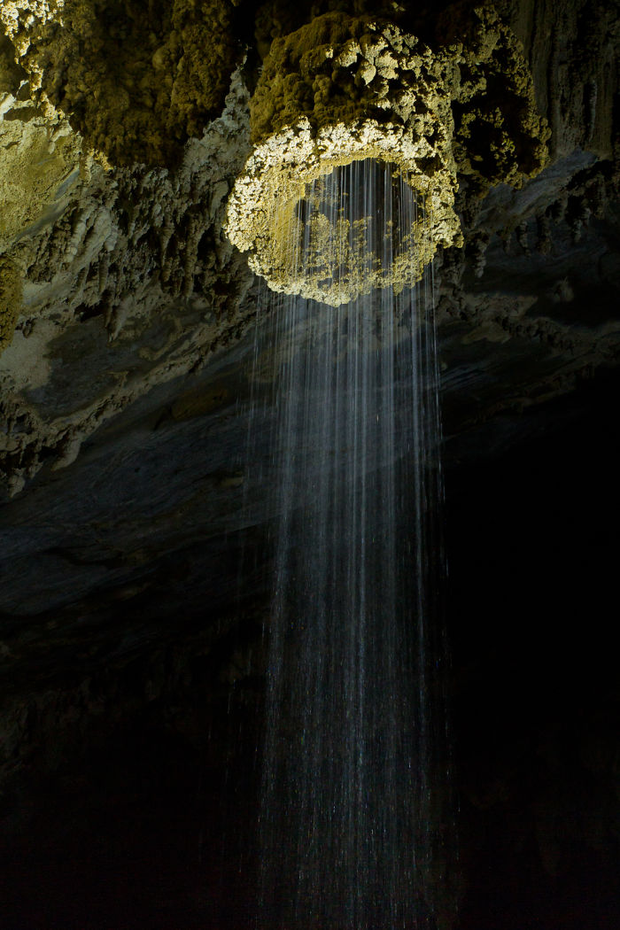 Waterfall cascading through a hole in rocky cave ceiling showcasing beautiful caves from around the world.