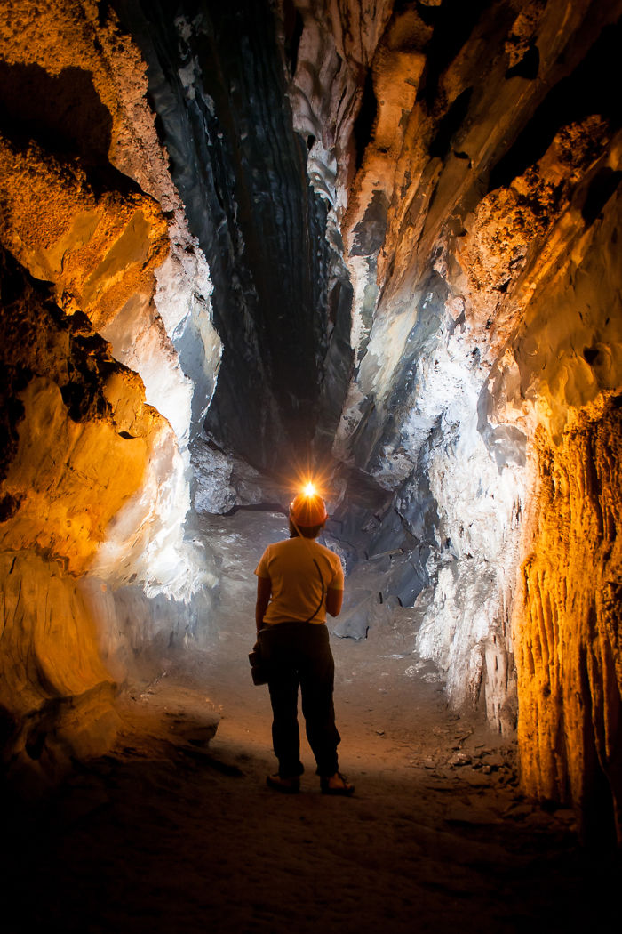 Person exploring a beautiful cave illuminated by headlamp light, surrounded by textured rock formations inside.