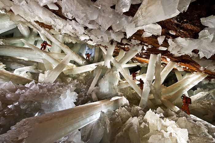 Explorers inside a beautiful cave filled with giant crystal formations showcasing stunning natural geological beauty.
