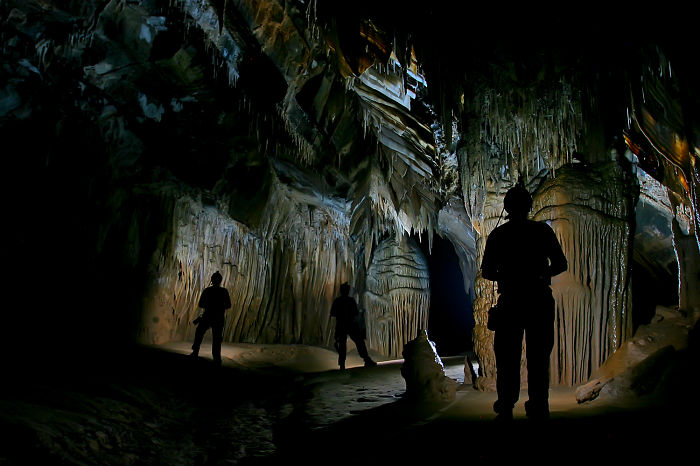 Explorers standing inside a beautiful cave with stunning stalactites and stalagmites, showcasing natural cave formations.