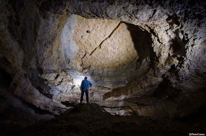 Person exploring inside a large, beautiful cave illuminated by a headlamp showcasing natural rock formations.