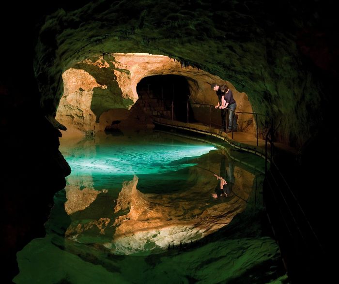 Person exploring a beautiful cave with illuminated turquoise water reflecting rocky cave walls and ceiling.