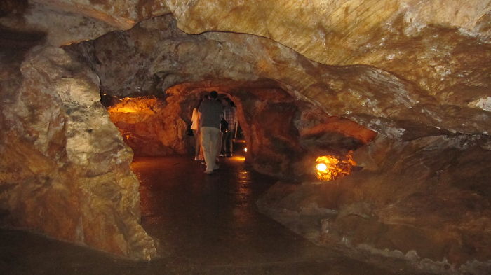 People exploring a beautiful cave interior with rocky walls and warm lighting along a pathway inside the cave.