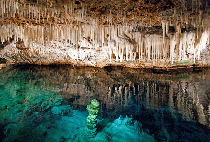 Stunning cave interior with clear blue water and numerous stalactites hanging from the ceiling in a natural underground cave.