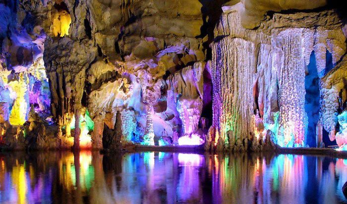 Colorfully lit beautiful cave interior with stalactites and stalagmites reflected in still underground water.