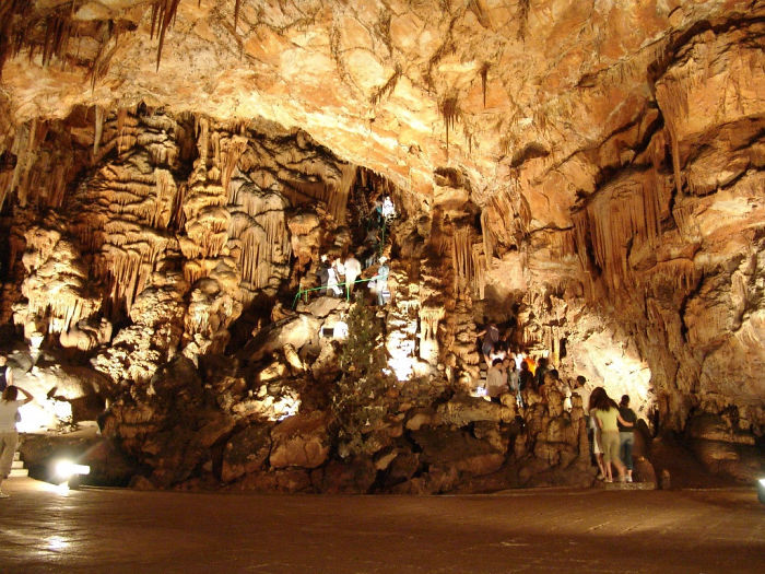 Visitors explore a large, beautifully illuminated cave interior with stunning rock formations and stalactites.