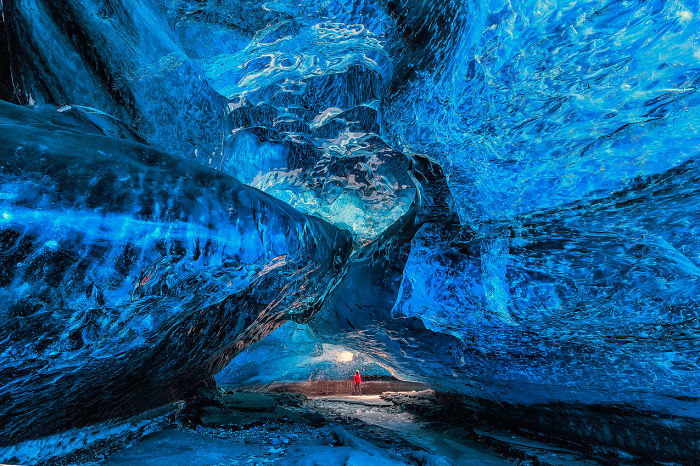 Stunning blue ice cave interior with a person exploring, showcasing the beauty of caves from around the world.