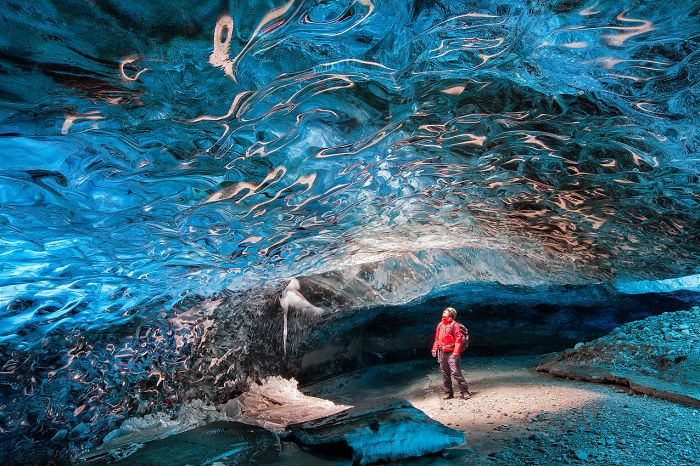 Person exploring a stunning blue ice cave with intricate patterns on the ceiling in a beautiful natural cave formation.