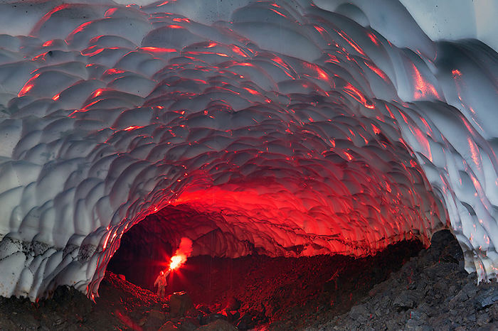 Person holding a red flare inside a beautiful cave with textured white ceiling and rocky floor, showcasing natural formations.