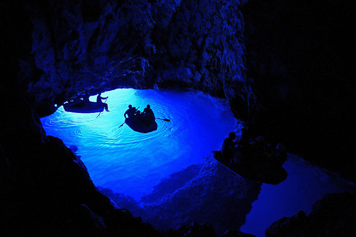 Visitors in boats exploring a beautiful cave with glowing blue water, showcasing stunning natural cave formations.