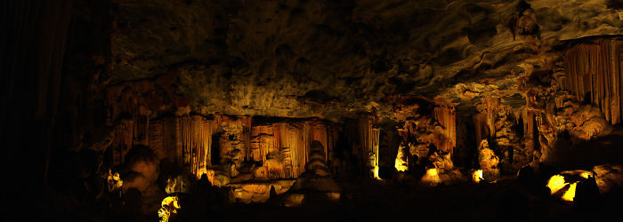 Panoramic view of a beautifully illuminated cave interior with stalactites and stalagmites formations.