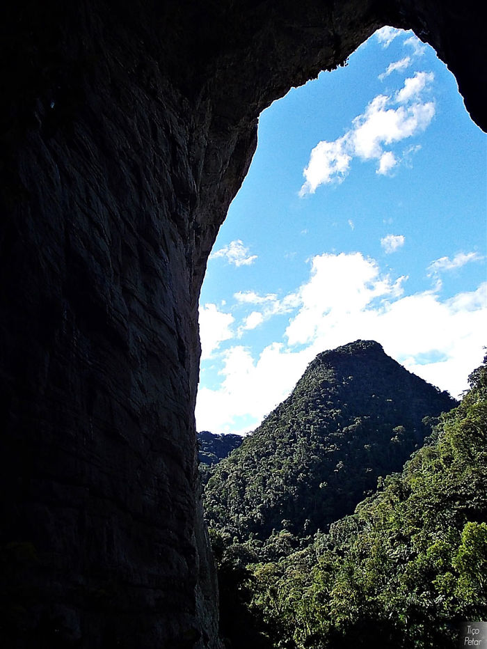 View from inside a beautiful cave looking out towards forested mountains under a partly cloudy sky.