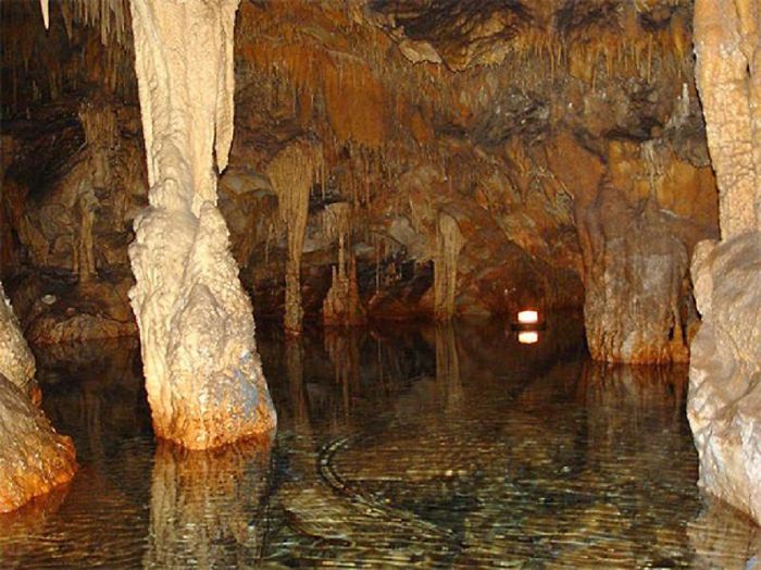 Underground cave with stalactites and stalagmites reflected in clear water, showcasing beautiful caves around the world.