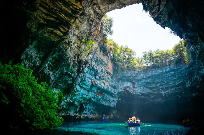 Boat with tourists exploring a beautiful cave surrounded by clear blue water and lush greenery inside the cave.