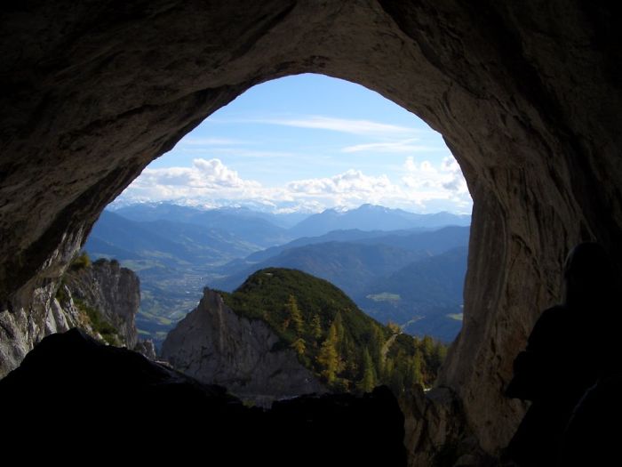 View from inside a beautiful cave showing mountains and a blue sky with clouds in the distance.