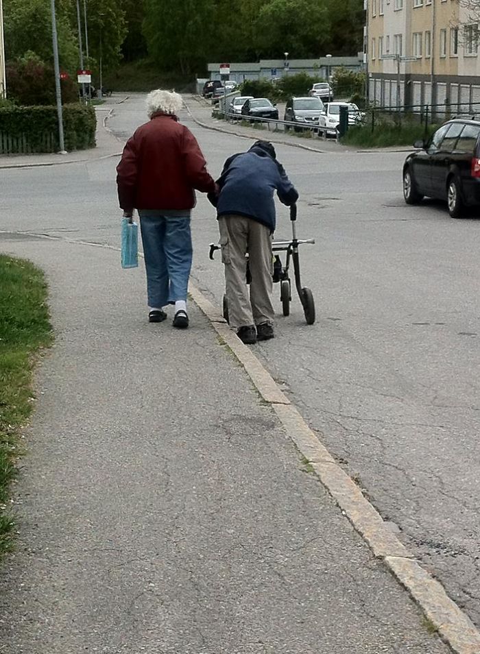 Elderly couple walking on a sidewalk, one using a walker, proving age doesn't limit fun.