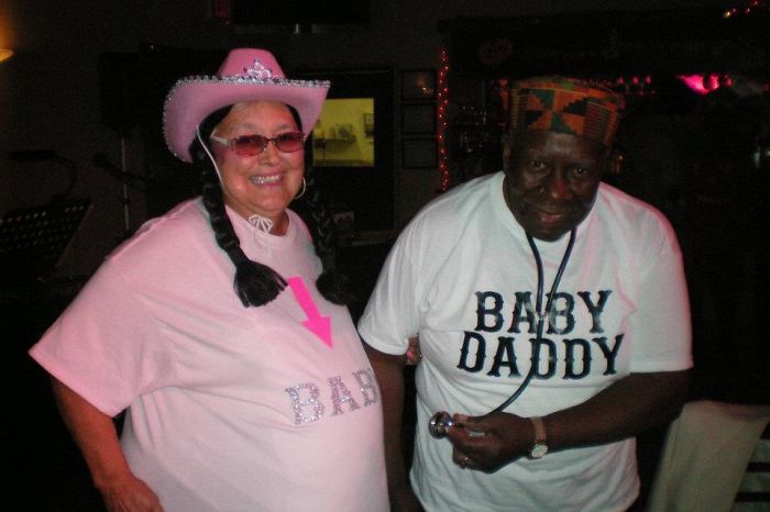 Elderly couple having fun, wearing humorous matching shirts and hats at a lively event.