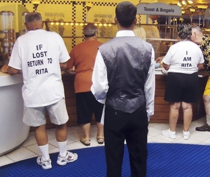 Elderly couple wearing humorous T-shirts at a buffet, with one saying "If lost return to Rita" and the other "I am Rita".