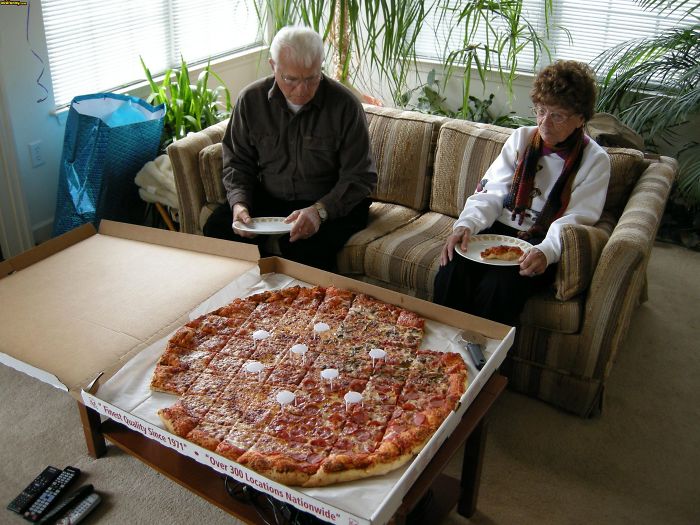 Elderly couple enjoying a giant pizza in a living room, showcasing older couples having fun.