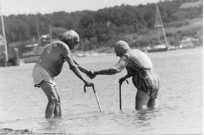 Elderly couple having fun wading through water with canes at the beach.