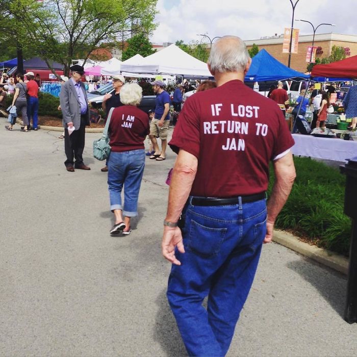 Elderly couple at a fair, wearing matching shirts with playful messages, enjoying their day out.