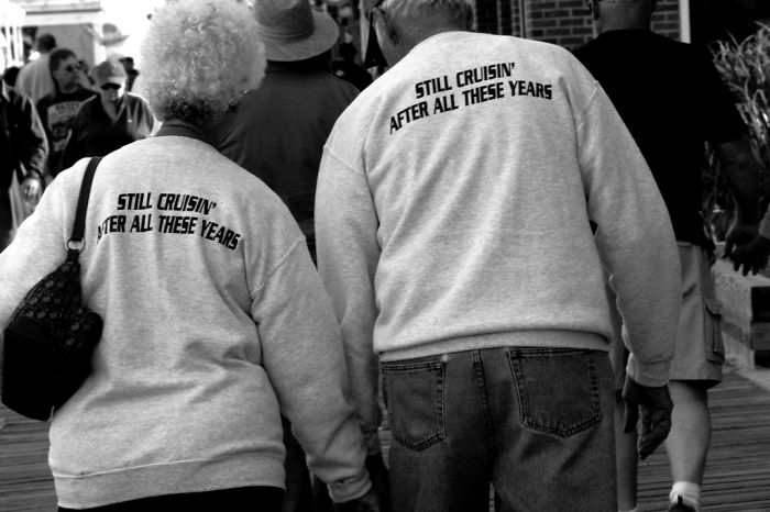 Elderly couple walking together, wearing matching shirts that say "Still Cruisin' After All These Years."