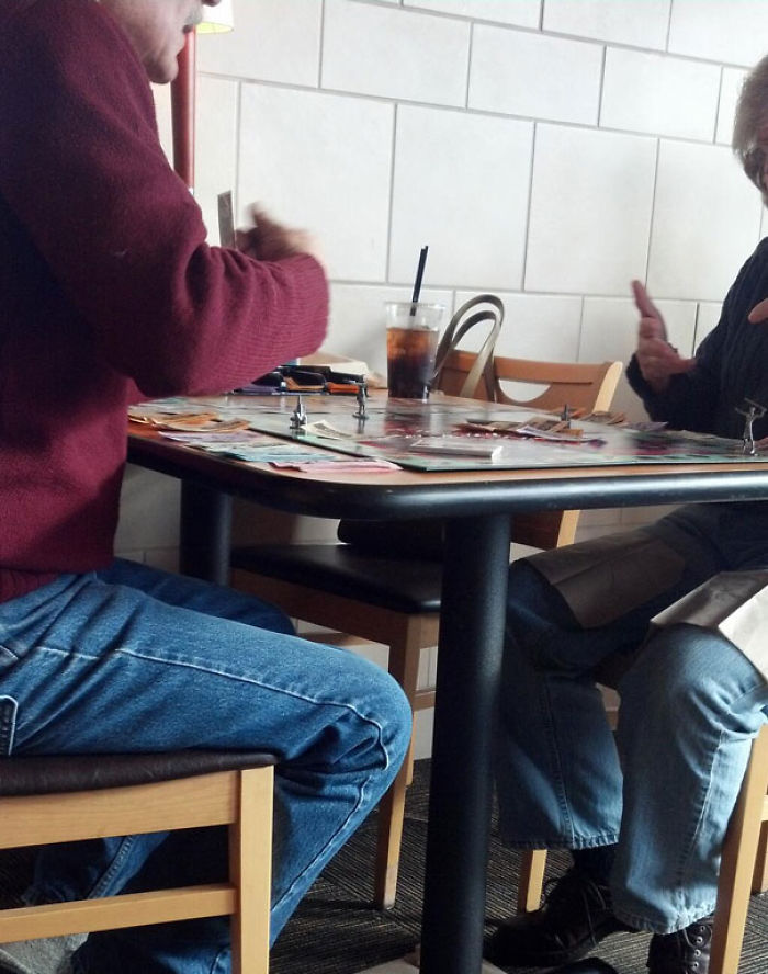 Elderly couple enjoying a board game at a table in a casual setting, showcasing their fun spirit.