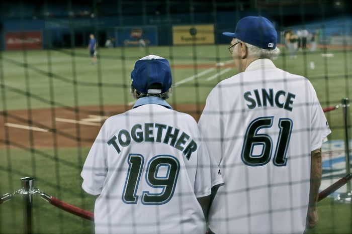 Elderly couple in matching baseball jerseys at a game, having fun together.
