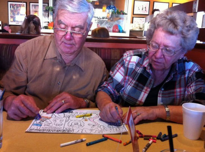 Elderly couple having fun coloring together at a restaurant table.