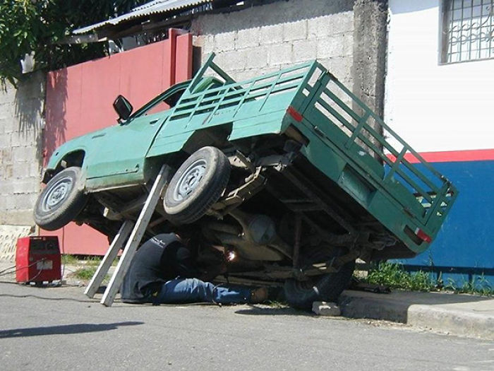 Man under precariously propped truck, illustrating why women live longer.