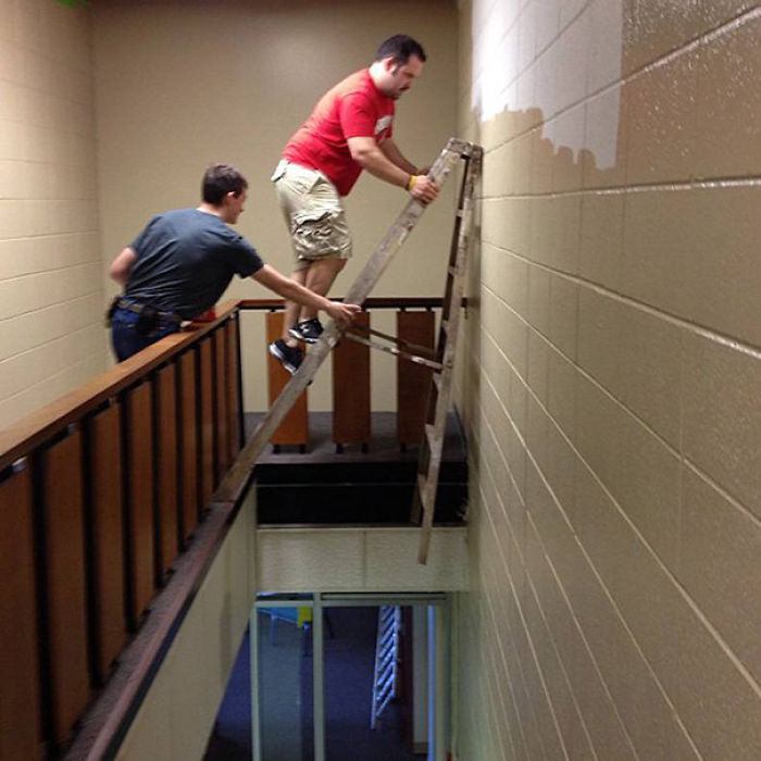 Two men balancing a ladder dangerously over a stairway, illustrating why women live longer than men.