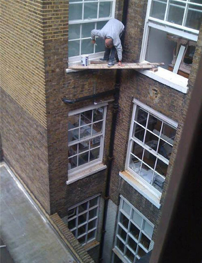 Man balancing on a wooden plank between windows, illustrating risky behavior related to why women live longer than men.