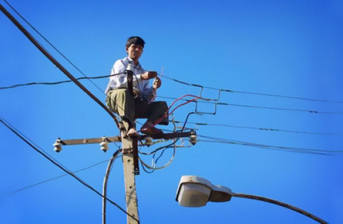Man balancing on a power pole, handling wires, indicating risky behavior related to why women live longer than men.