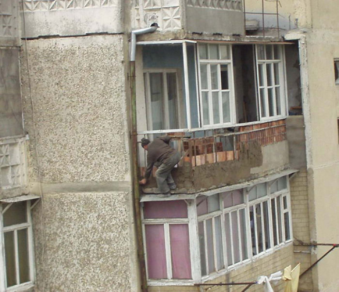 Man doing dangerous work on a high-rise balcony, illustrating one reason women live longer than men.