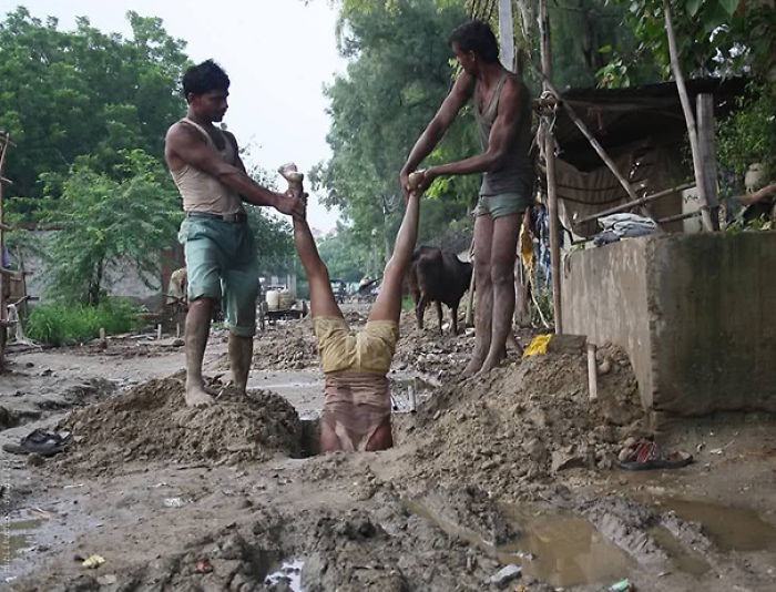 Two men holding a third person upside down in muddy ground, illustrating why women might live longer than men.
