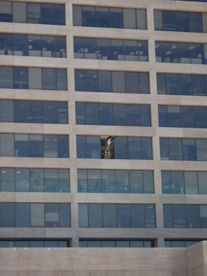 Man on ladder in open high-rise window, illustrating safety risks and why women live longer than men.