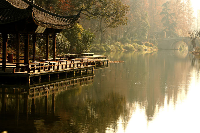 Traditional Chinese pavilion by a calm lake surrounded by autumn trees, showcasing serene nature in China travel.