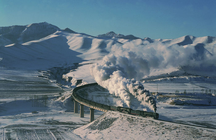 Steam train crossing a bridge in snowy mountains capturing the beauty of travel in China as a top reason to visit.