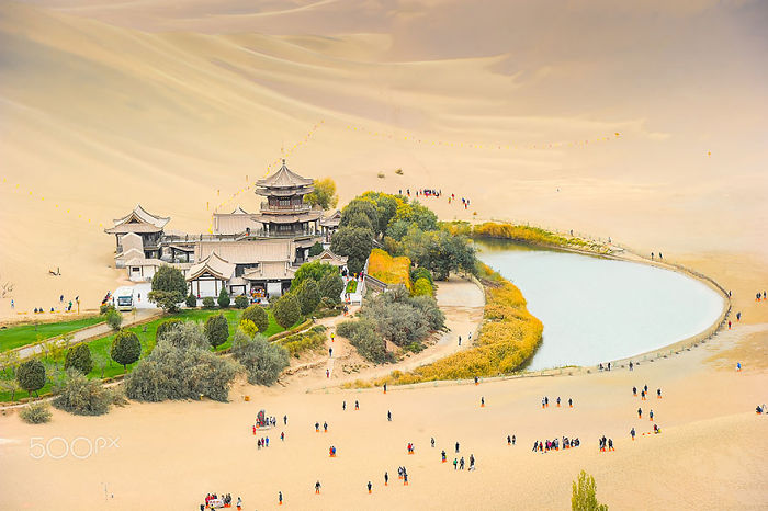 Ancient Chinese architecture and crescent lake surrounded by desert, attracting visitors showcasing reasons to visit China.