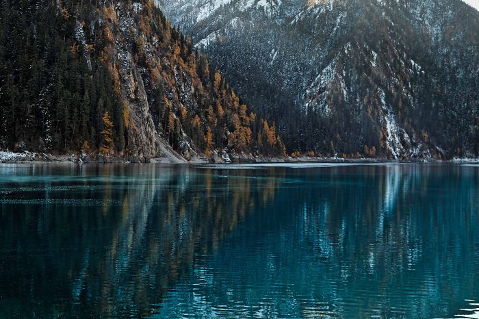 Scenic lake surrounded by snow-covered mountains and autumn trees, showcasing natural beauty to visit in China.