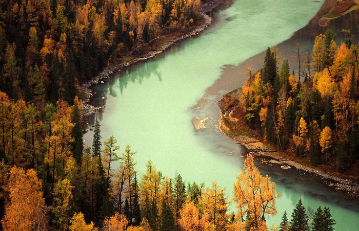 Scenic river winding through dense forest with autumn-colored trees showcasing natural beauty to visit in China