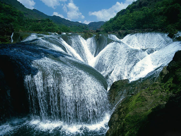 Wide waterfall flowing over rocks surrounded by lush greenery showcasing reasons to visit China nature attractions