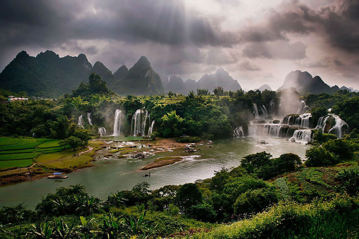 Scenic waterfalls and lush greenery with karst mountains under dramatic clouds showcasing nature in China travel destinations.