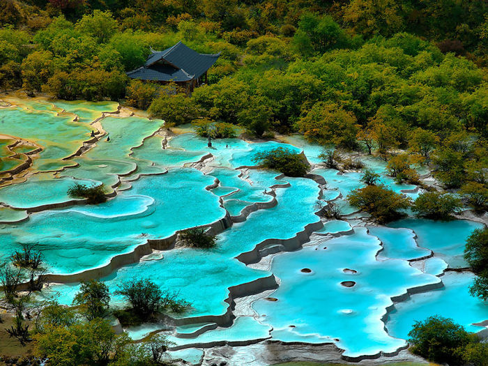 Terraced turquoise pools surrounded by autumn trees and a traditional building, showcasing reasons to visit China.