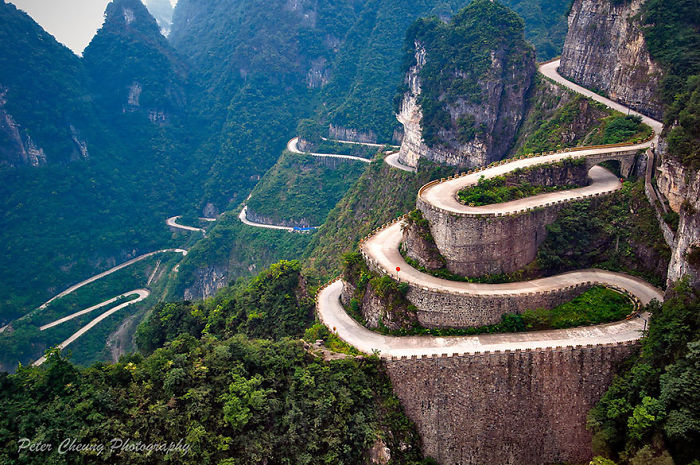 Winding mountain road in China surrounded by lush greenery and steep cliffs showcasing reasons to visit China.