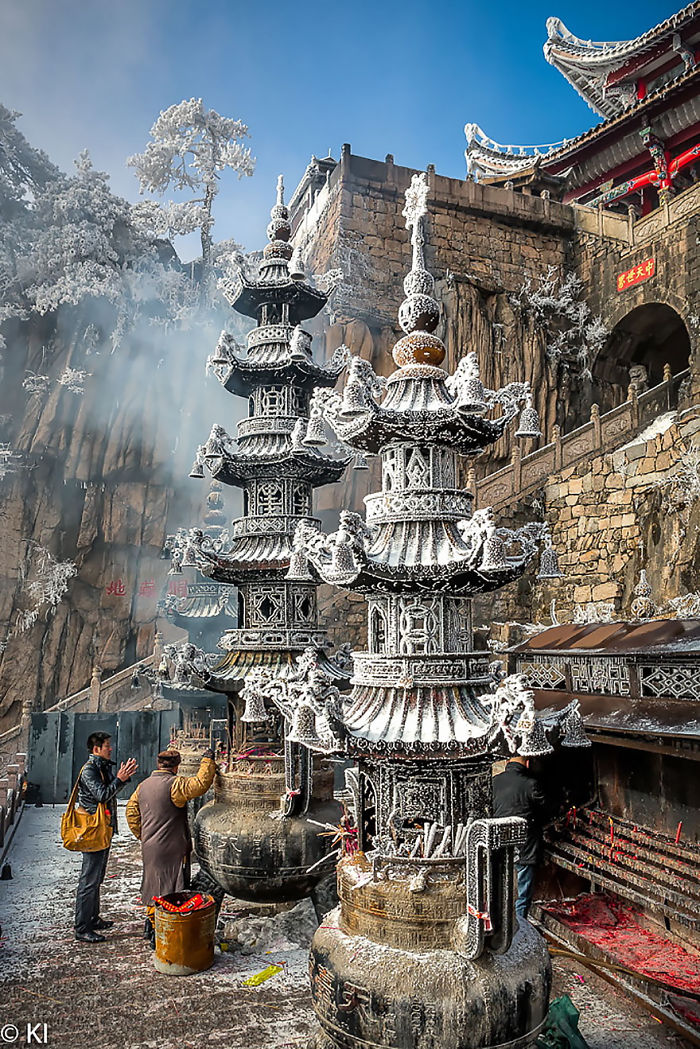 Ancient temple scene in China with visitors and intricate stone pagodas covered in white frost or smoke.